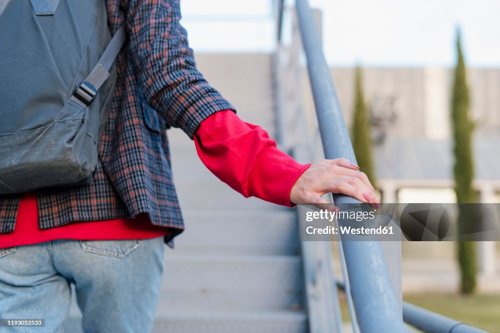 Crop view of young woman with backpack walking upstairs