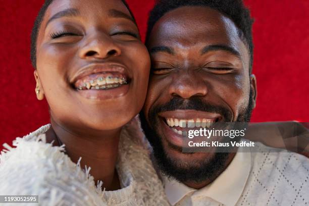 smiling friends with eyes closed against red wall - braces and smiles fotografías e imágenes de stock