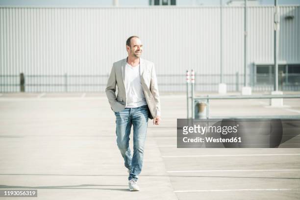 happy mature businessman walking on parking deck - mann frontal ganzkörper jacket stock-fotos und bilder