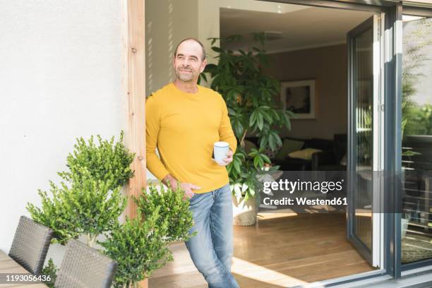 mature man standing at terrace door at home with coffee cup - 50 sombras fotografías e imágenes de stock