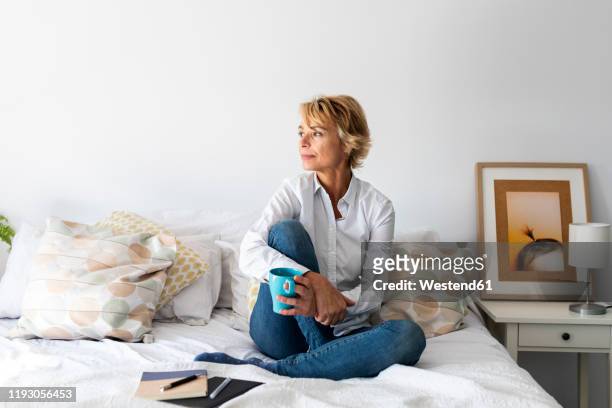 relaxed mature woman sitting on bed at home - 50 54 years stock pictures, royalty-free photos & images