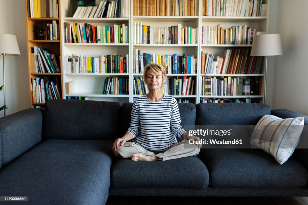 Mature woman practicing yoga on couch at home
