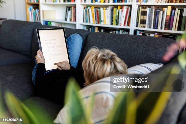 mature woman relaxing on couch at home using graphics tablet - back cushion stock pictures, royalty-free photos & images