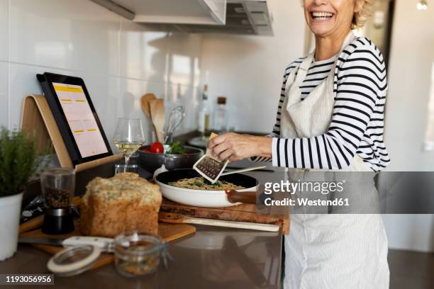 happy mature woman with tablet cooking pasta dish in kitchen at home - one pot pasta stock-fotos und bilder