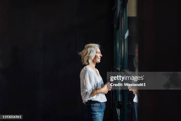 casual mature businesswoman looking out of window in loft office - casual woman pensive side view stockfoto's en -beelden