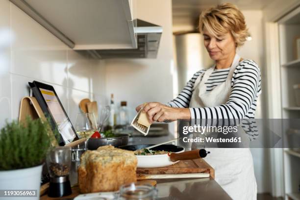 mature woman with tablet cooking pasta dish in kitchen at home - kochen stock-fotos und bilder