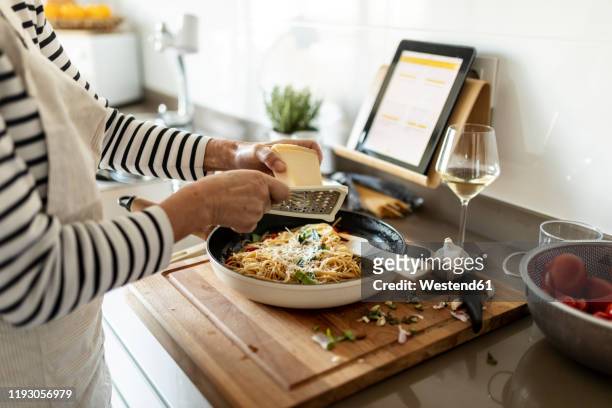close-up of woman with tablet cooking pasta dish in kitchen at home - râpe à fromage photos et images de collection