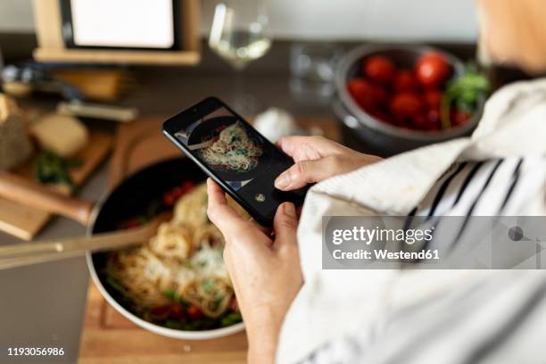 close-up of woman taking smartphone picture of her pasta dish in kitchen at home - woman cooking phone stock-fotos und bilder