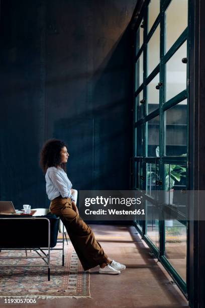 young businesswoman looking out of window in loft office - business woman looking through window stock pictures, royalty-free photos & images