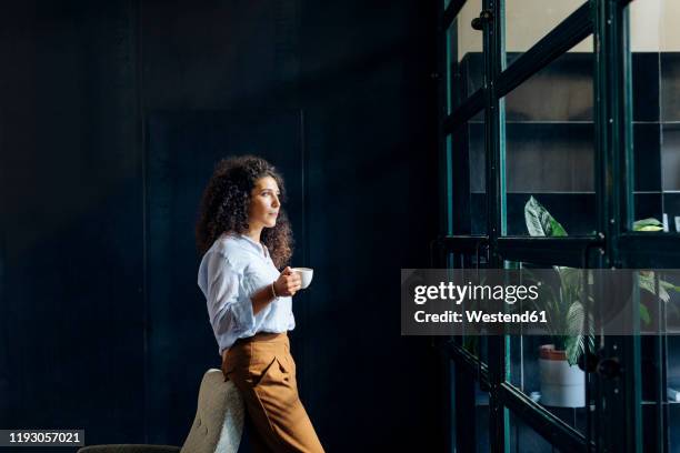 young businesswoman looking out of window in loft office - belgium people stock pictures, royalty-free photos & images