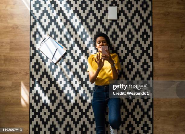 young woman lying on carpet at home using smartphone - black pattern photos et images de collection