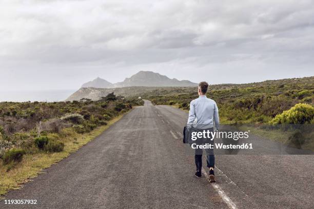 back view of businessman walking on country road, cape point, western cape, south africa - cape point stock pictures, royalty-free photos & images