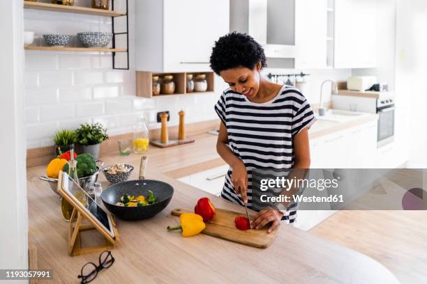 young woman with tablet cooking in kitchen at home cutting vegetables - striped shirt stock pictures, royalty-free photos & images