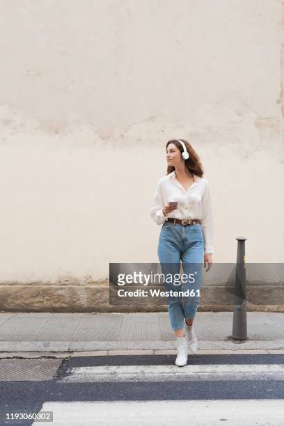 young woman with smartphone and headphones crossing the street - borne tactile photos et images de collection