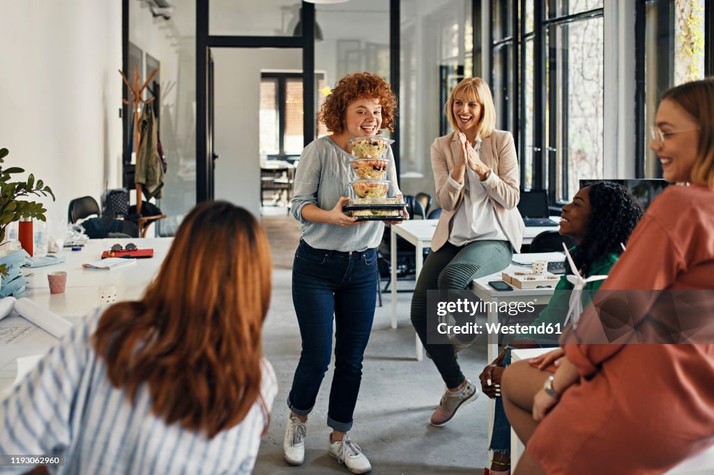 Happy businesswoman serving takeaway food to colleagues in office