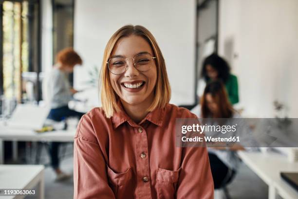 portrait of a happy businesswoman in office with colleagues in background - happy laugh stockfoto's en -beelden
