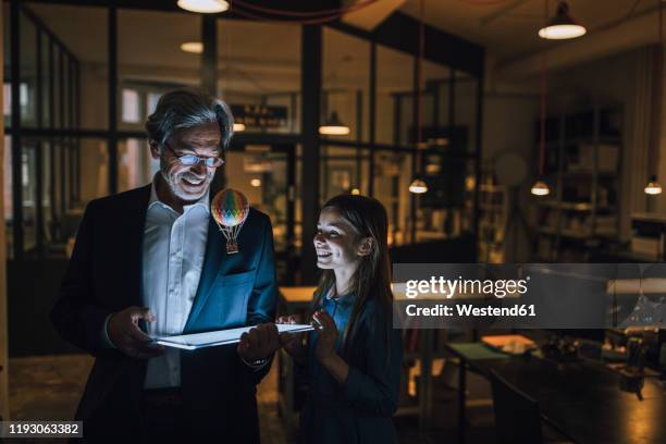 happy senior buisinessman and girl with hot-air balloon and shining tablet in office - fantasy portrait stock-fotos und bilder