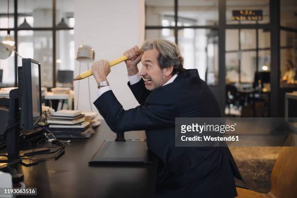 angry senior businessman with giant pencil at desk in office - person surrounded by computer screens stock pictures, royalty-free photos & images