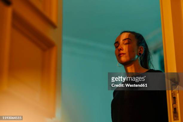 young woman with closed eyes in shadow and light at open door - eyes closed stock-fotos und bilder