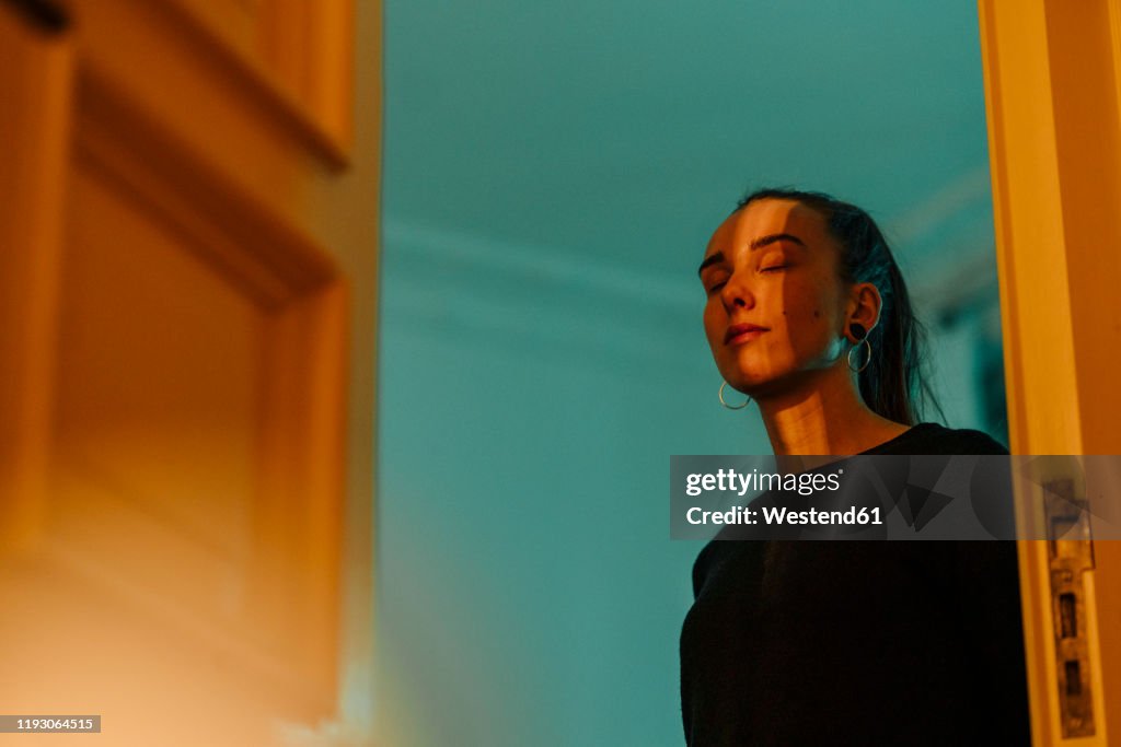 Young woman with closed eyes in shadow and light at open door