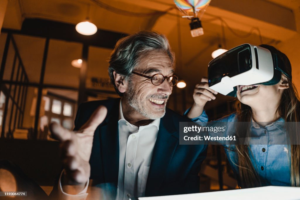 Happy senior buisinessman and girl wearing VR glasses with hot-air balloon in office