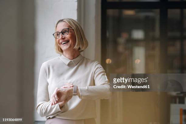 happy mature businesswoman at the window in office - smart watch stock pictures, royalty-free photos & images