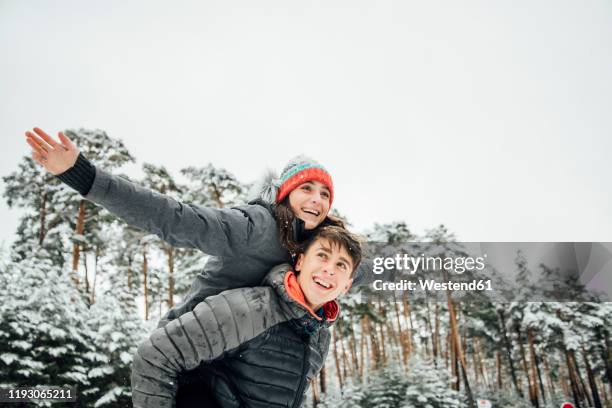 portrait of smiling young man giving his happy girlfriend a piggyback ride in winter forest - arms outstretched stock pictures, royalty-free photos & images