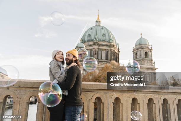 happy young couple embracing watching soap bubbles in the city, berlin, germany - berlin cathedral stock-fotos und bilder