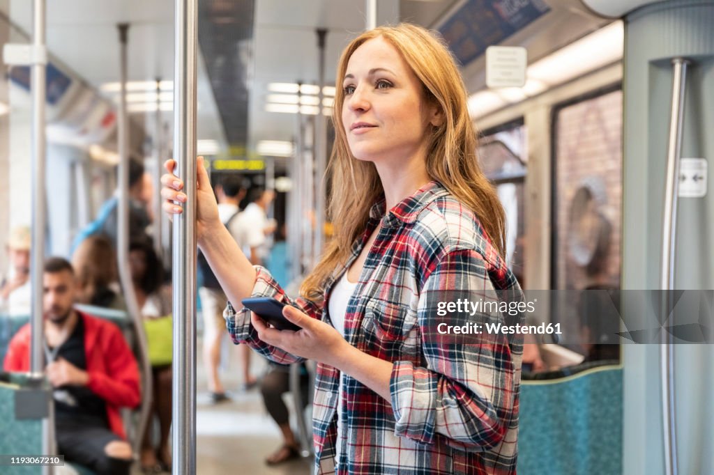 Smiling woman with smartphone on the subway, Berlin, Germany