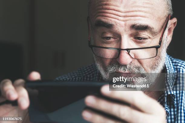 senior man using smartphone at home - suspicion stock-fotos und bilder