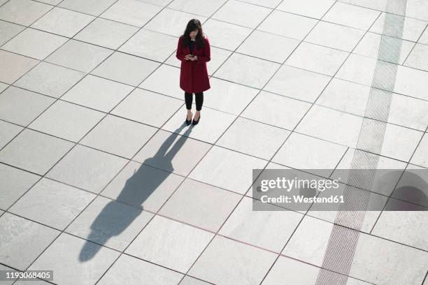 businesswoman using smartphone and standing on concrete floor - sombra longa sombra imagens e fotografias de stock