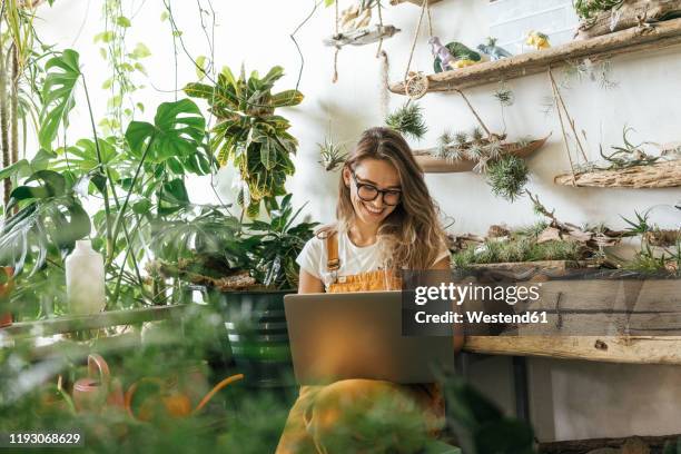 happy young woman using laptop in a small gardening shop - independent stockfoto's en -beelden