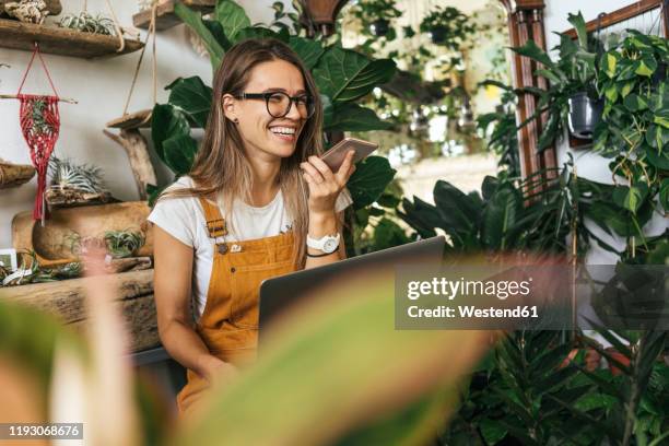 happy young woman using smartphone in a small gardening shop - einzelhandelsberuf stock-fotos und bilder