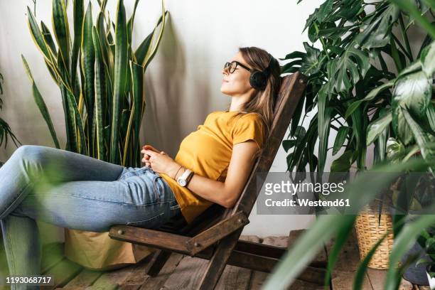 relaxed young womansitting in chair listening to music at home - attività del fine settimana foto e immagini stock