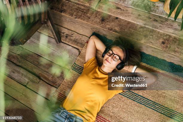 relaxed young woman lying on the floor at home listening to music - hände hinter dem kopf stock-fotos und bilder