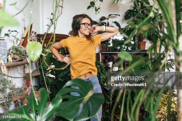 cheerful young woman surrounded by plants listening to music with headphones - circondare foto e immagini stock
