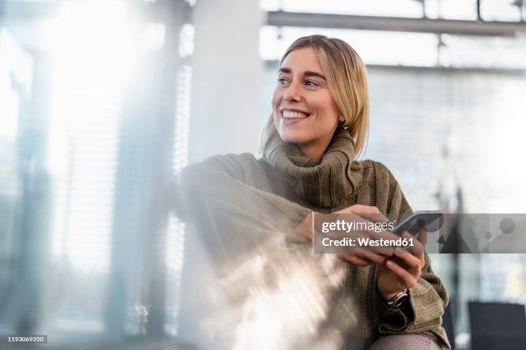 Smiling young woman with cell phone sitting in waiting area looking around