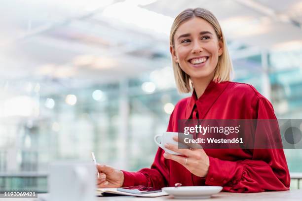 happy young businesswoman taking notes in a cafe - red shirt stock pictures, royalty-free photos & images