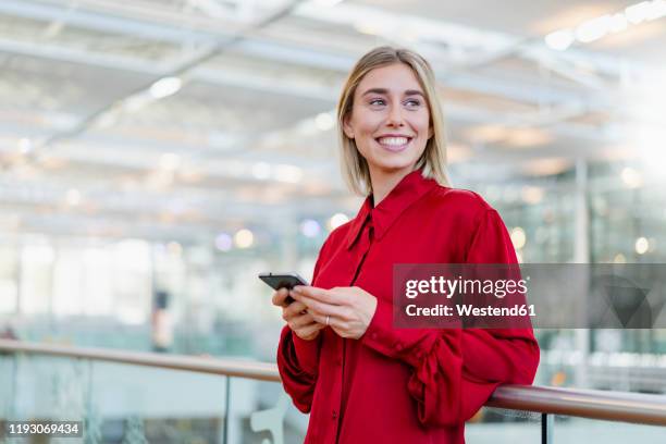 smiling young businesswoman standing at a railing with cell phone - looking around stock pictures, royalty-free photos & images
