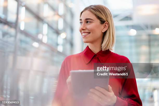 smiling young businesswoman wearing red shirt using tablet - erwartung stock-fotos und bilder