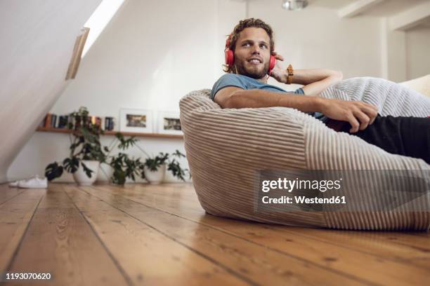 young man relaxing in beanbag at home listening to music - junger mann allein stock-fotos und bilder