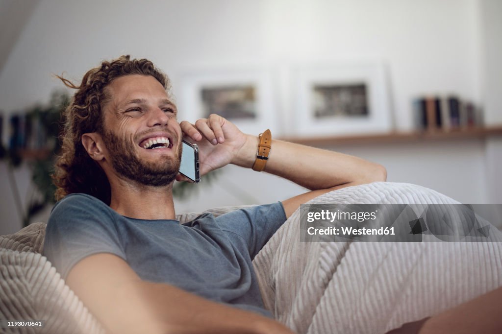 Laughing young man relaxing in beanbag at home talking on the phone
