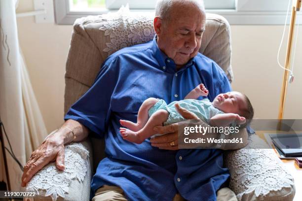 grandfather sitting in an armchair holding a newborn baby - baby grandpa imagens e fotografias de stock