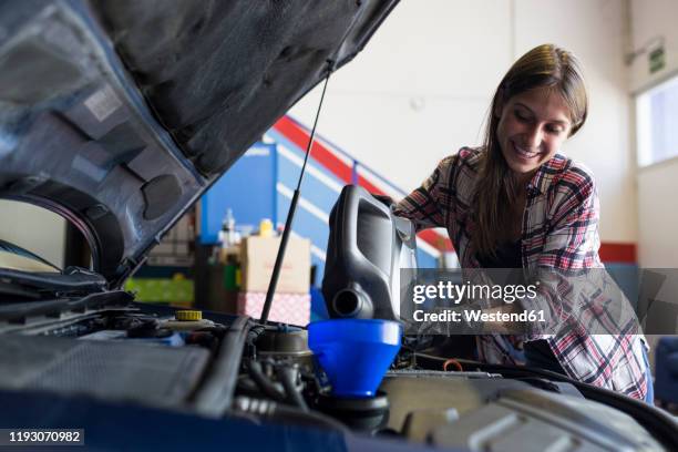 smiling casual woman in gloves holding can of engine oil and pouring it through funnel into car working in service - lubrication stock pictures, royalty-free photos & images
