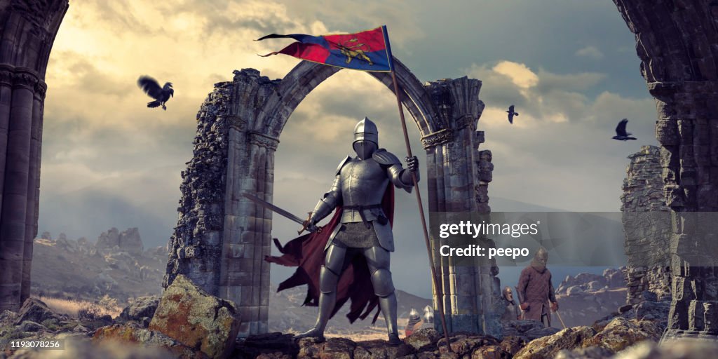 Cavaliere medievale in armatura con bandiera e spada vicino alle rovine