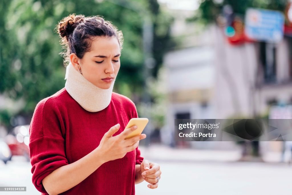 Woman in neck brace using mobile phone on street