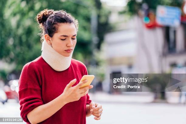 woman in neck brace using mobile phone on street - cervical collar stock pictures, royalty-free photos & images