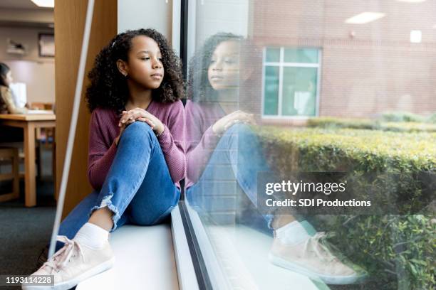 young girl daydreams while looking out library window - african american girl child stock pictures, royalty-free photos & images