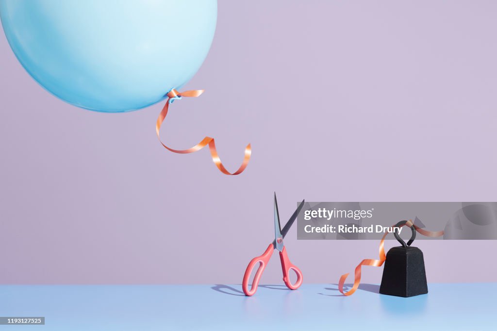 A pair of scissors cutting a balloon string to release the balloon