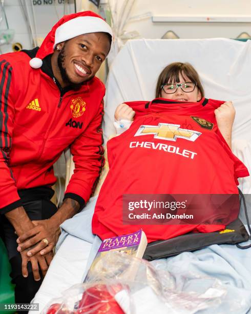 Diogo Dalot and Fred of Manchester United poses with Olivia during the club's annual Christmas hospital visits at Royal Manchester Children's...